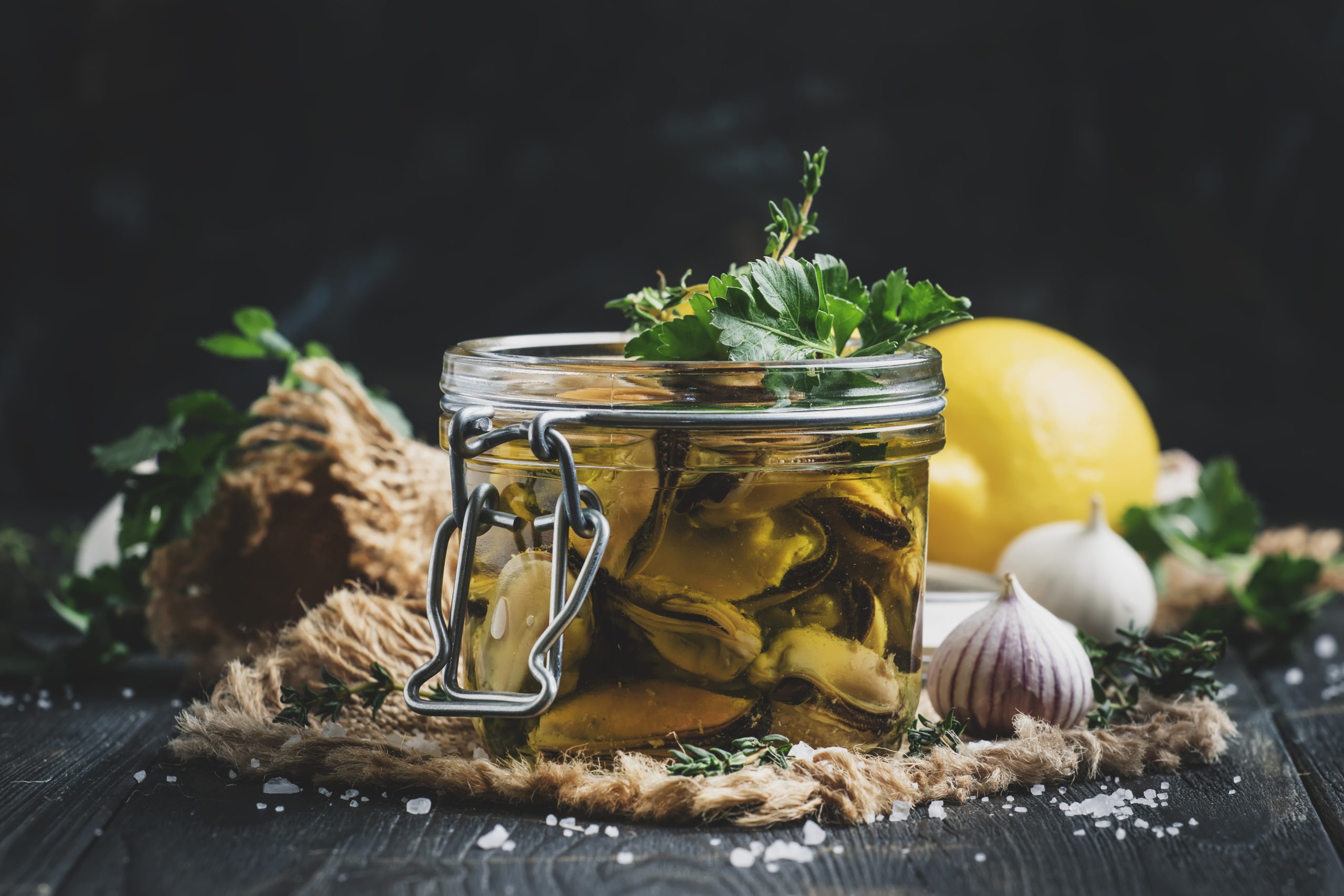 Canned mussels in olive oil and lemon juice with spices, garlic and herbs, black wooden kitchen table, selective focus